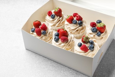 Photo of Tasty cupcakes with different berries in box on light grey table