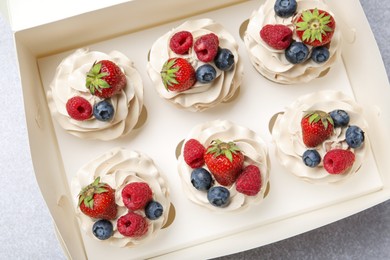 Photo of Tasty cupcakes with different berries in box on light grey table, top view