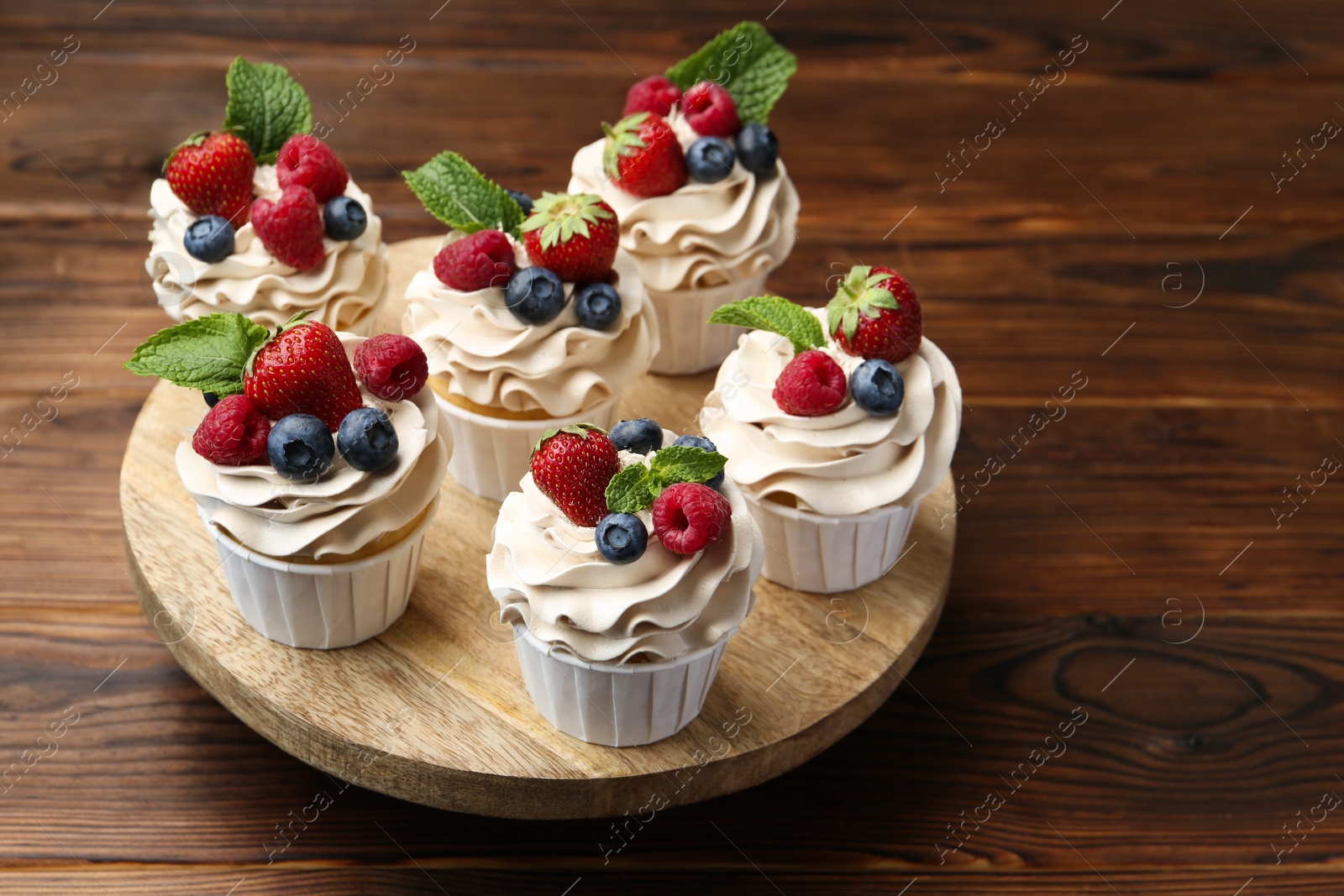 Photo of Tasty cupcakes with different berries and mint on wooden table