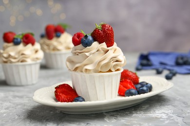 Photo of Tasty cupcakes with different berries on light grey table, closeup