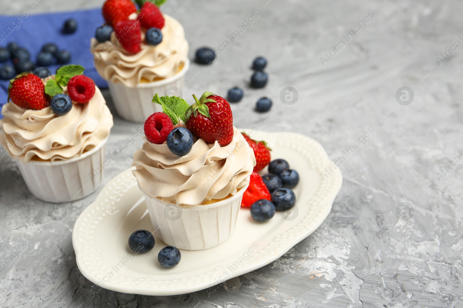 Photo of Tasty cupcakes with different berries and mint on light grey table, space for text