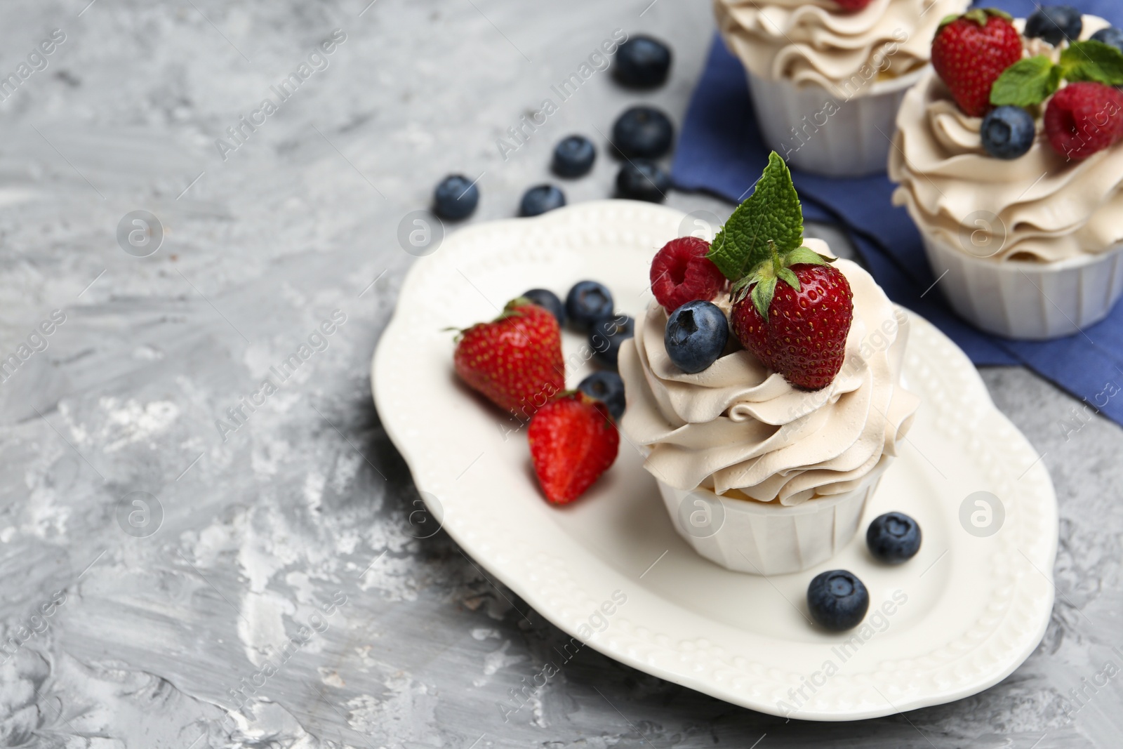 Photo of Tasty cupcakes with different berries and mint on light grey table, space for text