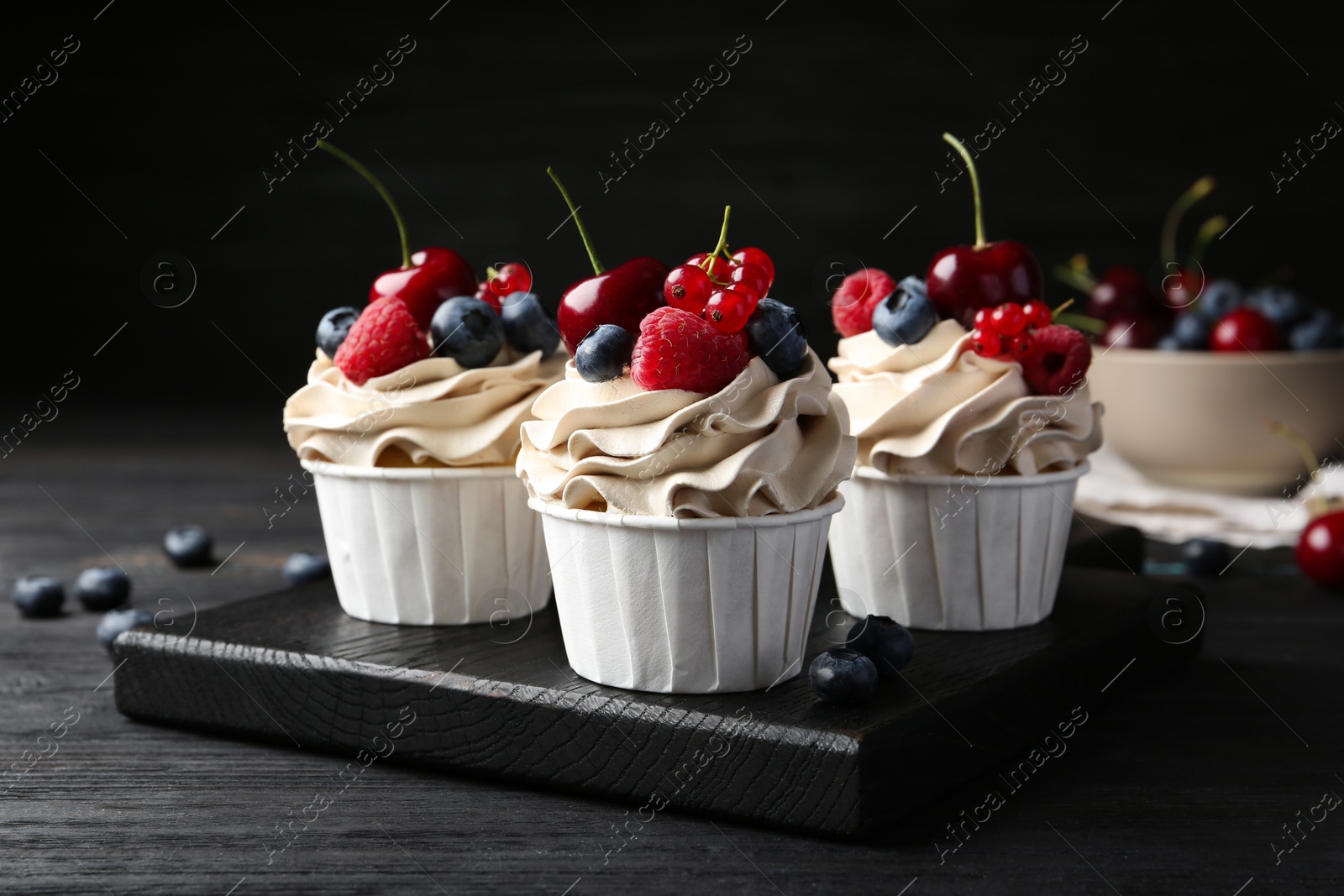 Photo of Tasty cupcakes with different berries on black wooden table, closeup