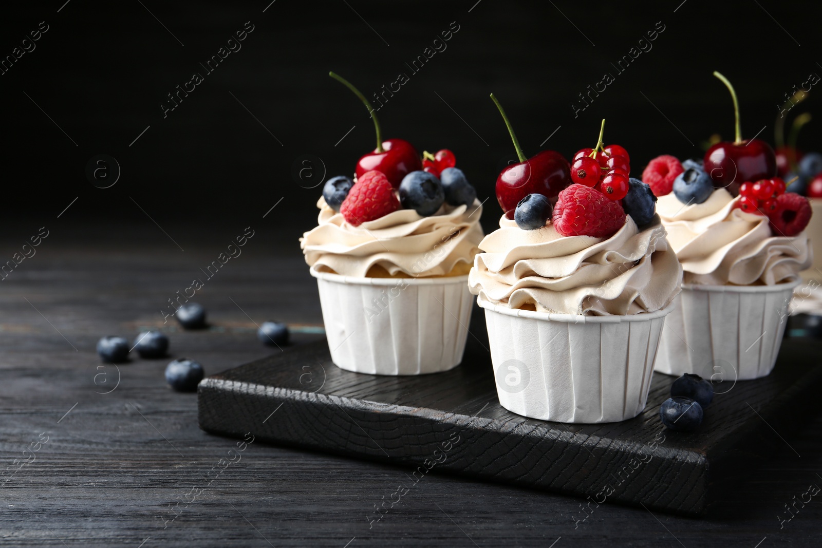 Photo of Tasty cupcakes with different berries on black wooden table, closeup. Space for text