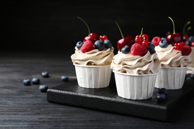 Photo of Tasty cupcakes with different berries on black wooden table, closeup. Space for text