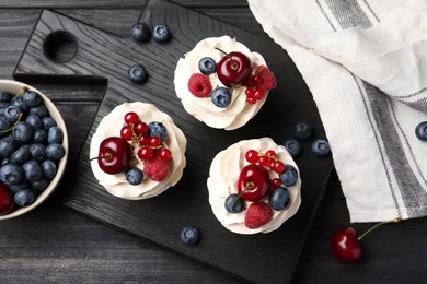 Photo of Tasty cupcakes with different berries on black wooden table, flat lay