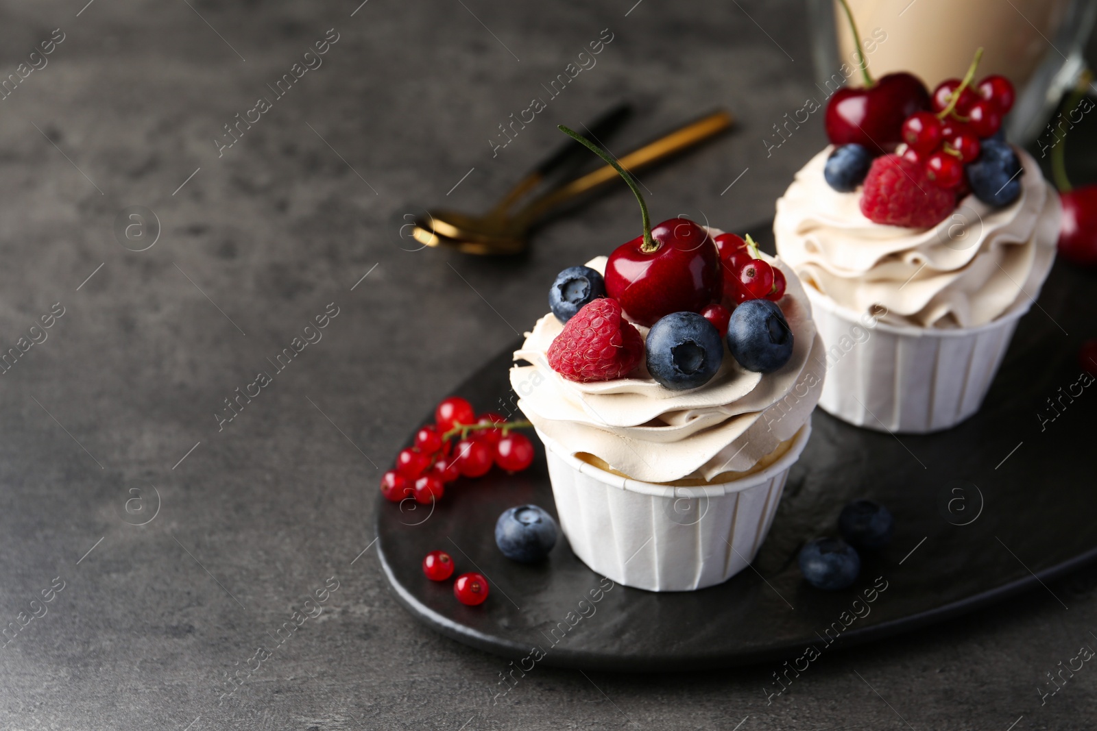 Photo of Tasty cupcakes with different berries on grey table, closeup. Space for text