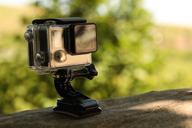 Photo of Modern action camera with mount on wooden surface outdoors, closeup. Space for text