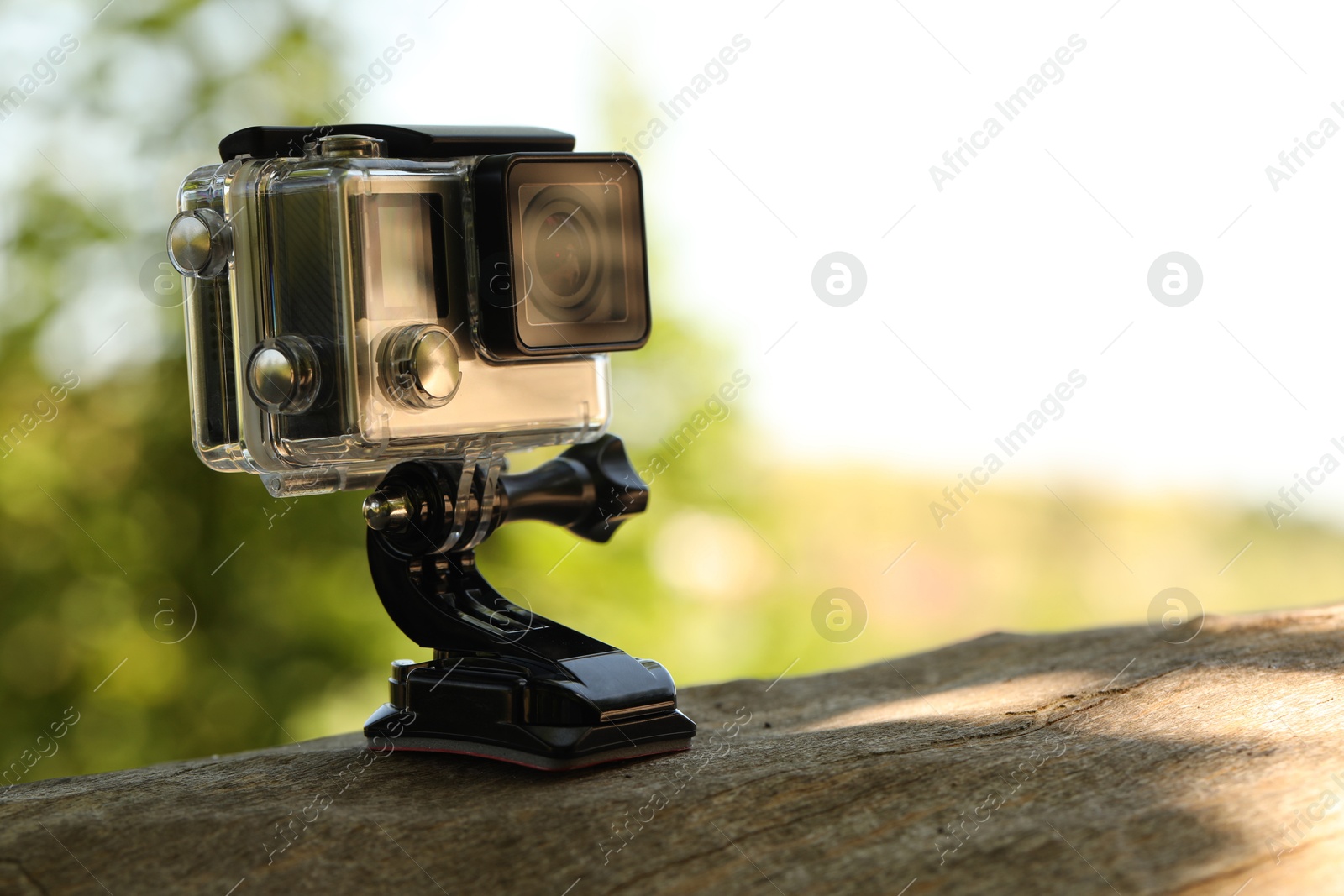 Photo of Modern action camera with mount on wooden surface outdoors, closeup. Space for text