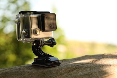 Modern action camera with mount on wooden surface outdoors, closeup. Space for text