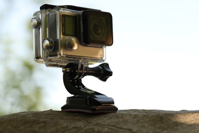 Modern action camera with mount on wooden surface outdoors, closeup