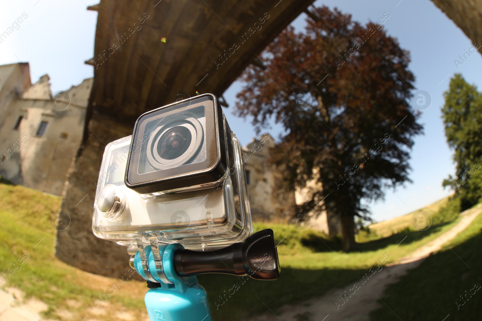 Photo of Modern action camera and monopod outdoors, space for text. Fisheye lens effect