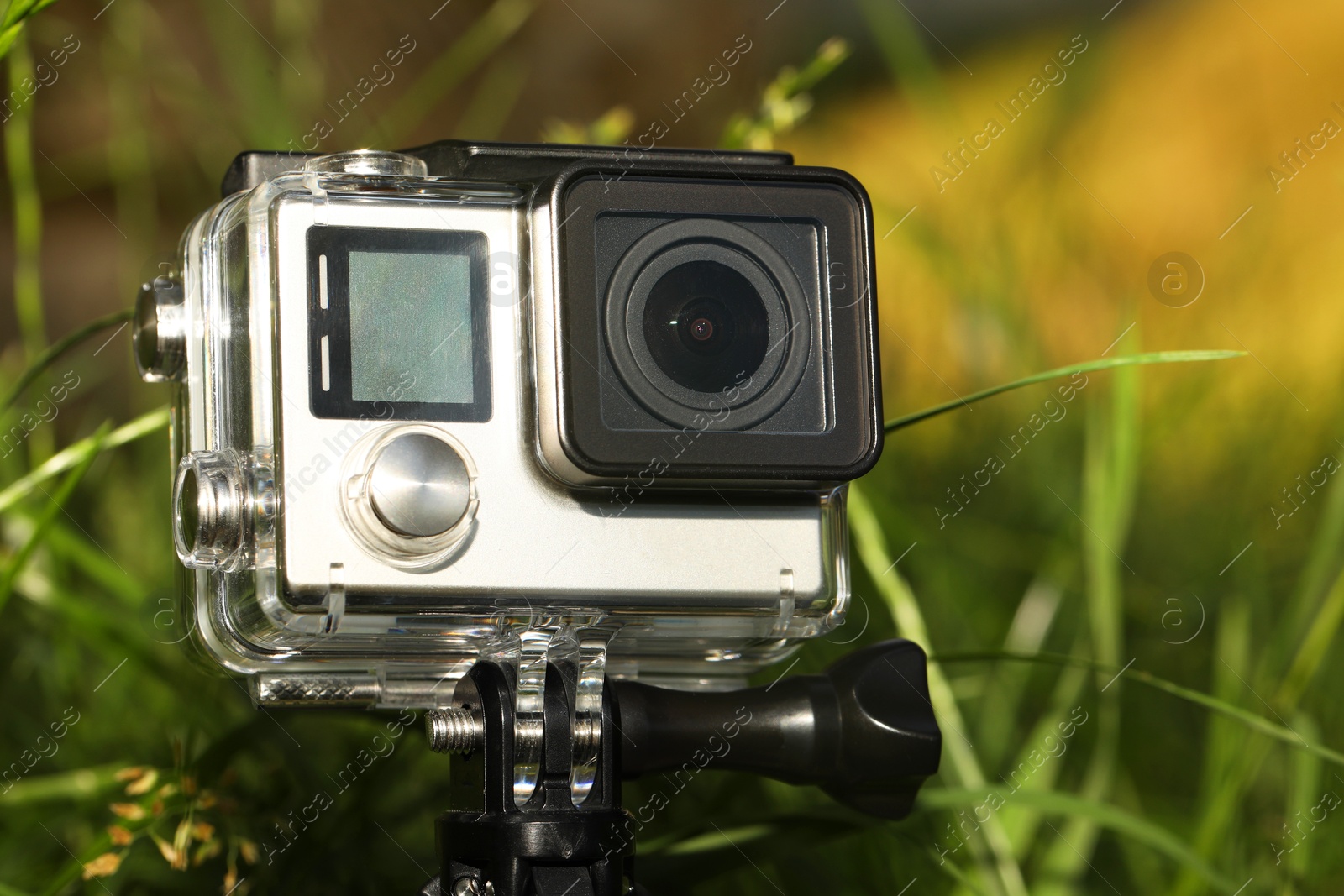 Photo of Modern action camera with tripod in grass outdoors, closeup