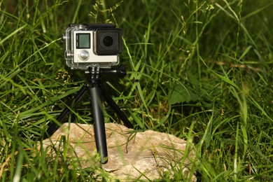 Photo of Modern action camera with tripod in grass outdoors. Space for text