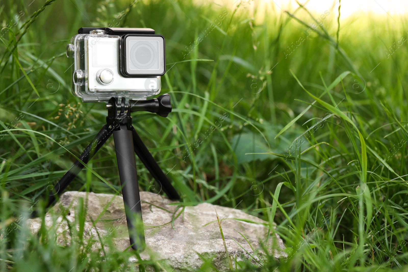 Photo of Modern action camera with tripod in grass outdoors. Space for text