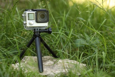 Photo of Modern action camera with tripod in grass outdoors. Space for text