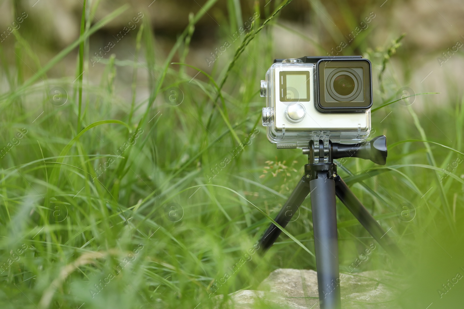 Photo of Modern action camera with tripod in grass outdoors. Space for text