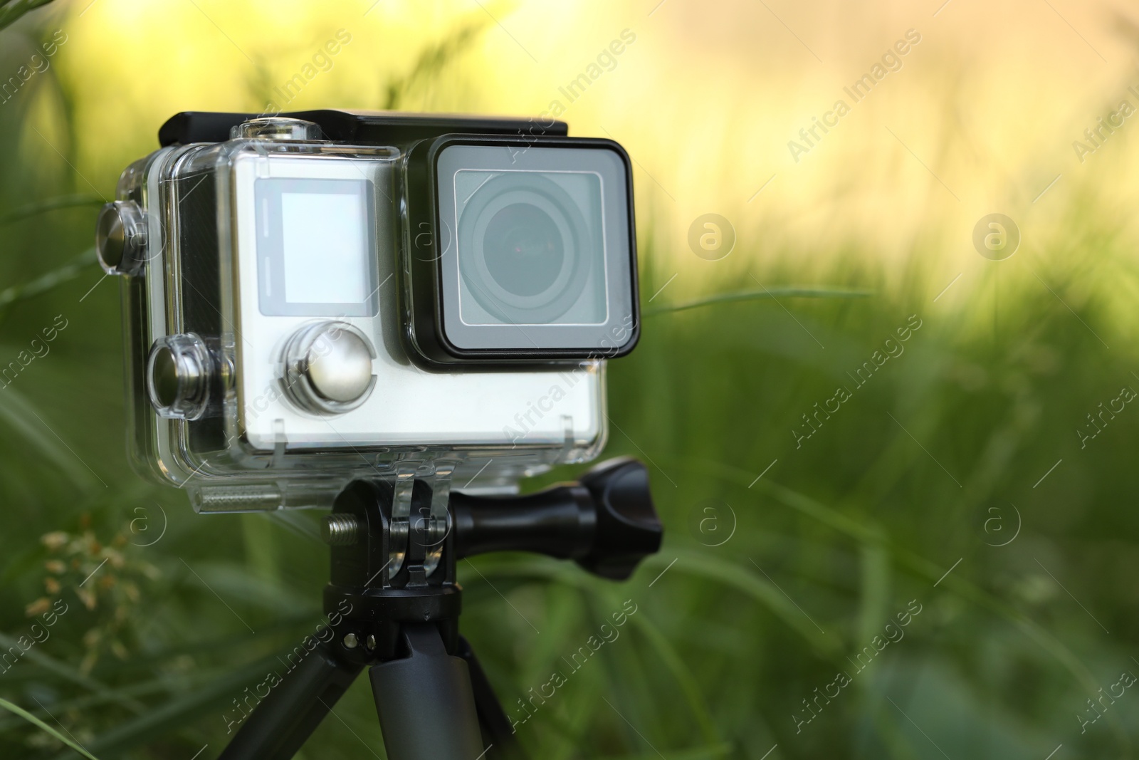 Photo of Modern action camera with tripod in grass outdoors, closeup. Space for text