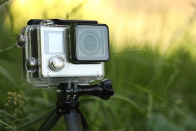 Modern action camera with tripod in grass outdoors, closeup. Space for text