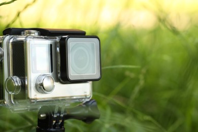 Modern action camera with tripod in grass outdoors, closeup. Space for text