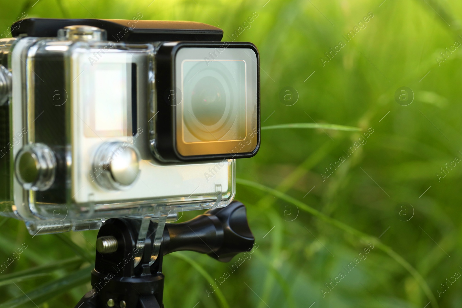 Photo of Modern action camera with tripod in grass outdoors, closeup. Space for text