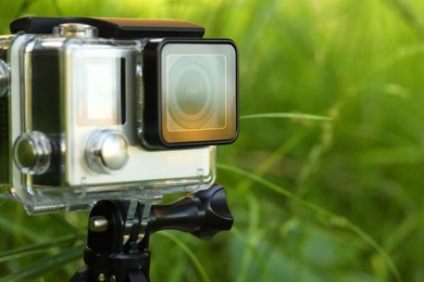 Modern action camera with tripod in grass outdoors, closeup. Space for text