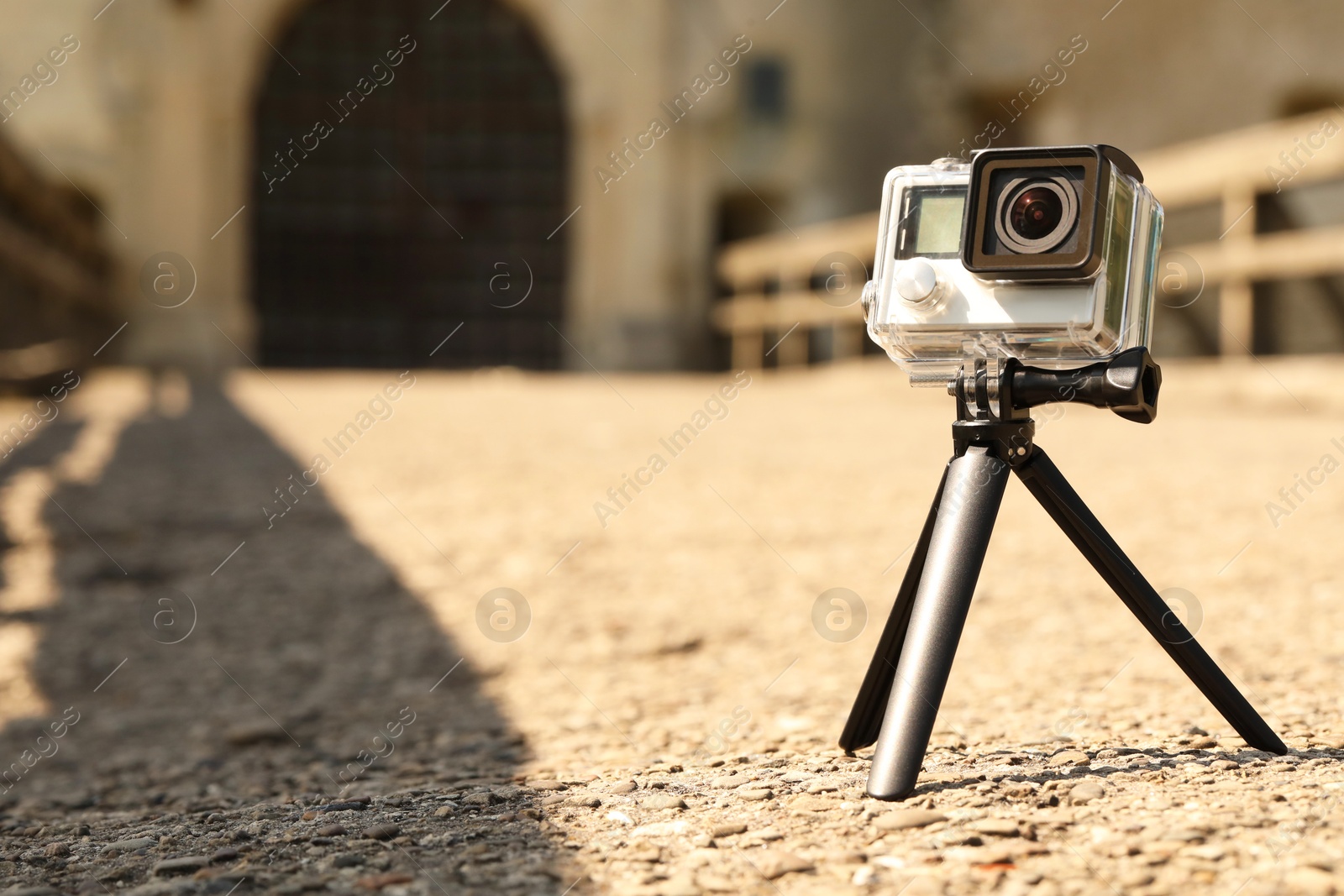 Photo of Modern action camera with tripod outdoors. Space for text