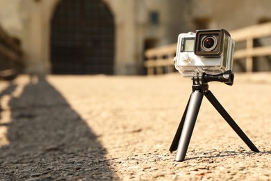 Modern action camera with tripod outdoors. Space for text