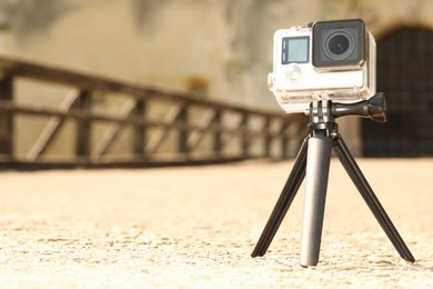 Photo of Modern action camera with tripod outdoors. Space for text