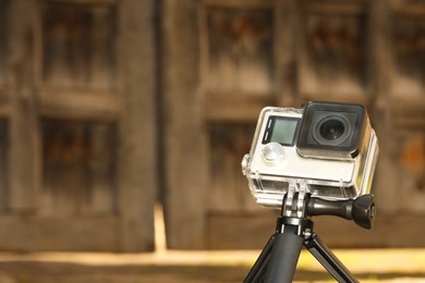 Modern action camera with tripod on blurred background, closeup. Space for text