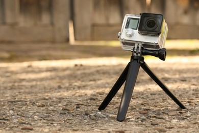 Photo of Modern action camera with tripod outdoors. Space for text