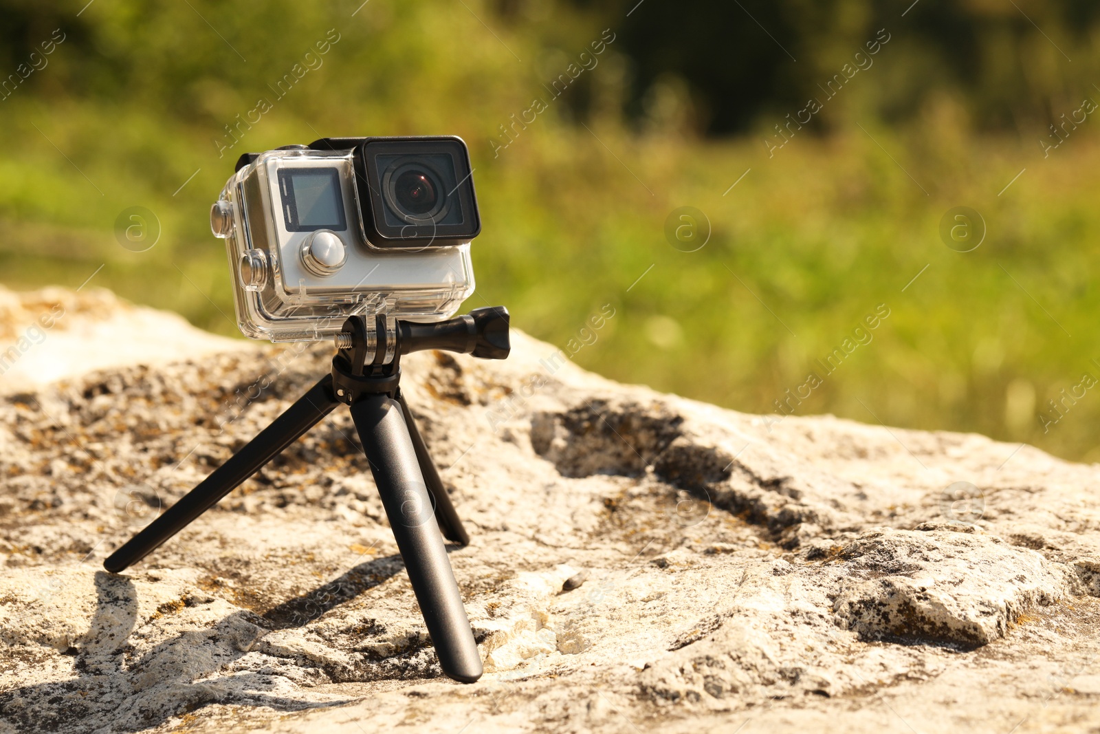 Photo of Modern action camera with tripod on stone outdoors, space for text