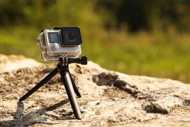 Modern action camera with tripod on stone outdoors, space for text