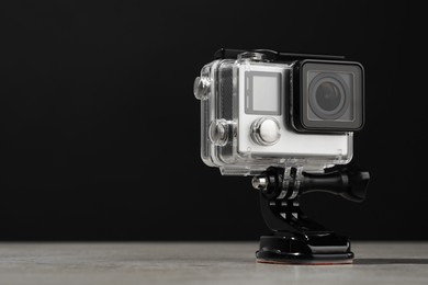 Photo of Modern action camera and mount on wooden table against black background. Space for text