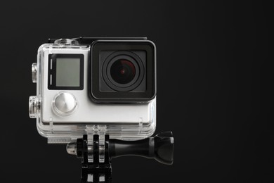 Photo of Modern action camera and mount against black background, closeup. Space for text