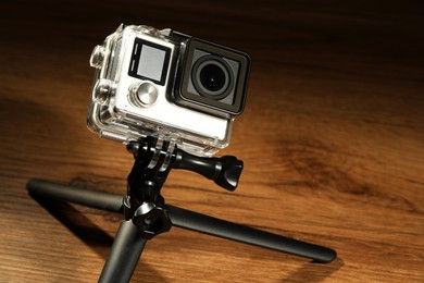 Modern action camera and tripod on wooden surface