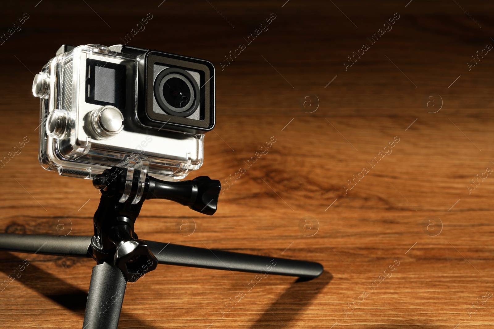 Photo of Modern action camera and tripod on wooden surface. Space for text