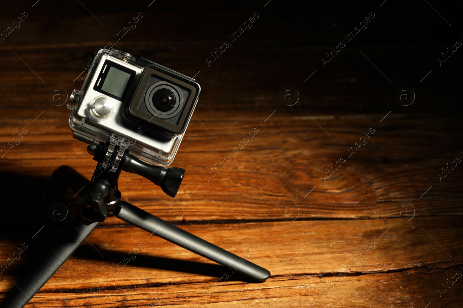 Photo of Modern action camera and tripod on wooden surface. Space for text