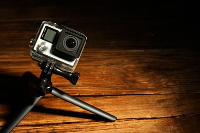 Modern action camera and tripod on wooden surface. Space for text