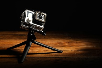 Modern action camera and tripod on wooden surface against black background. Space for text