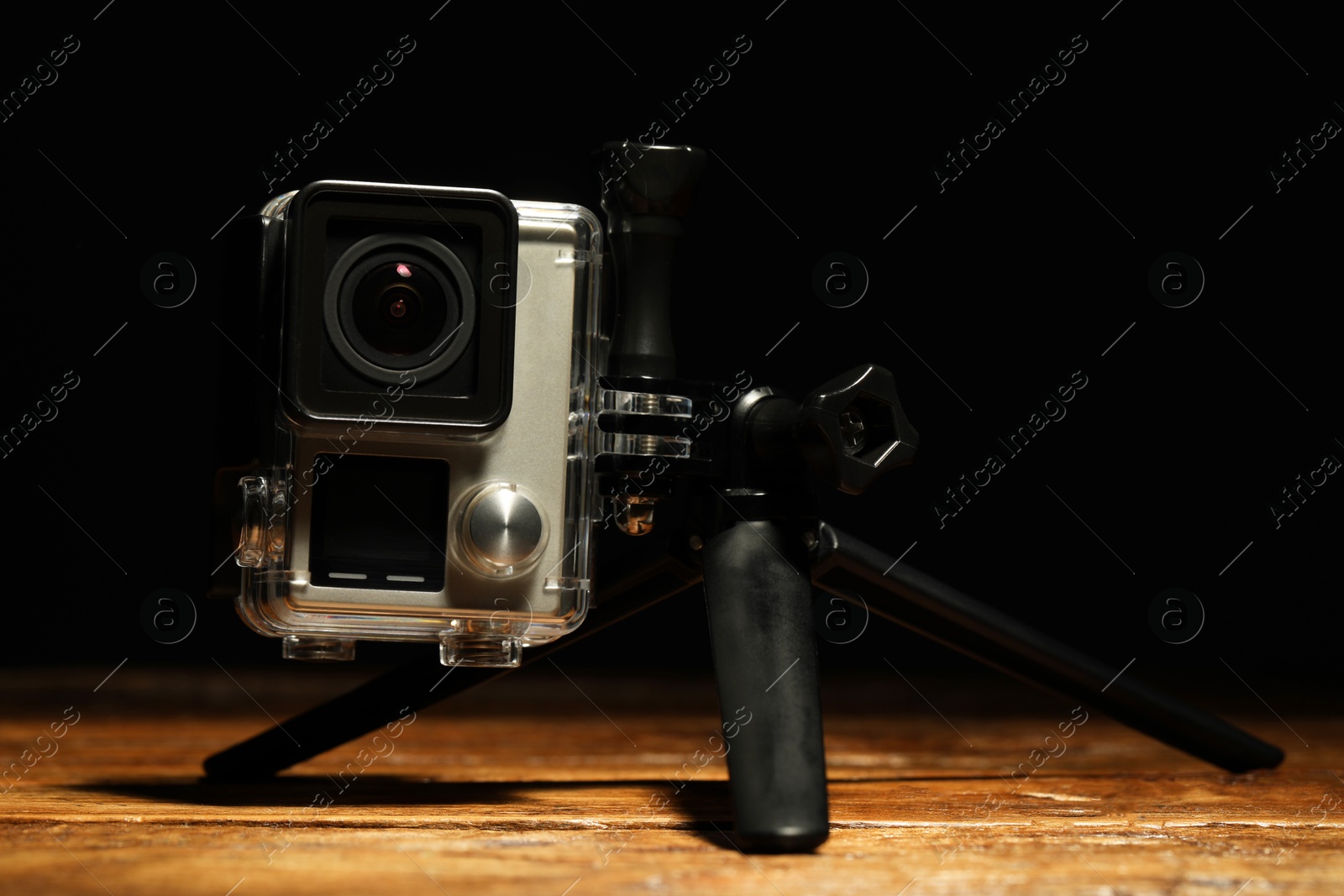 Photo of Modern action camera and tripod on wooden surface against black background