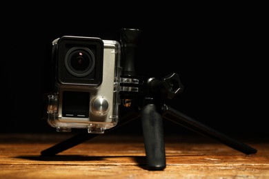 Photo of Modern action camera and tripod on wooden surface against black background