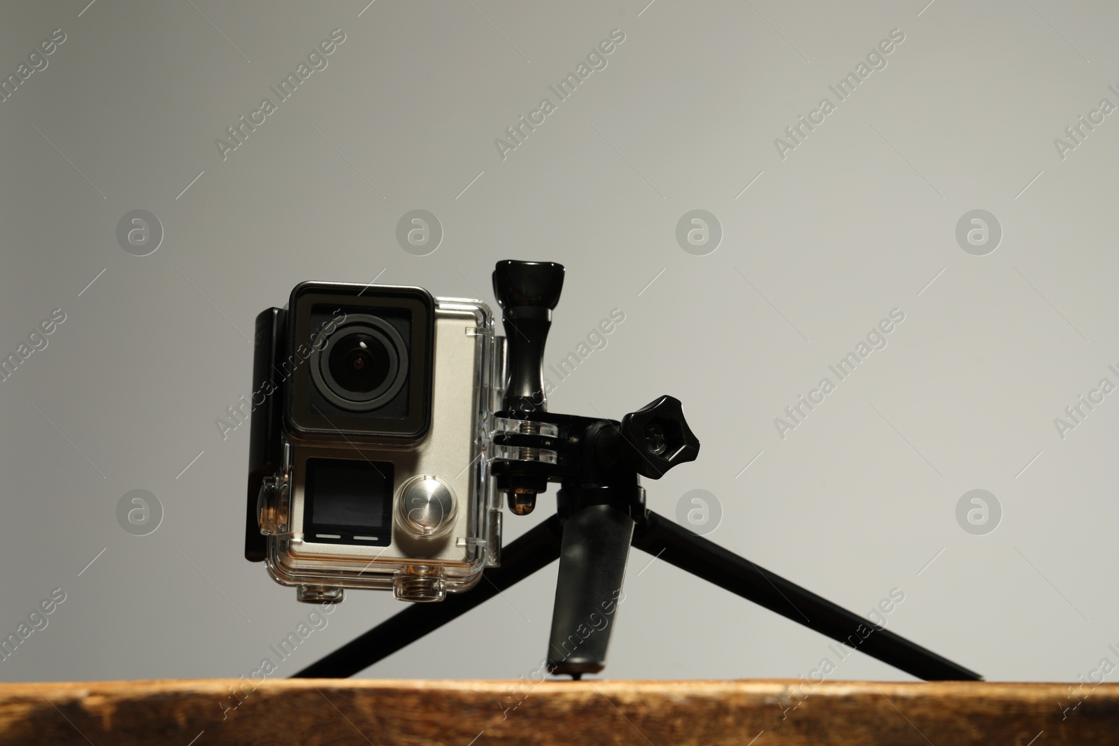 Photo of Modern action camera and tripod on wooden surface