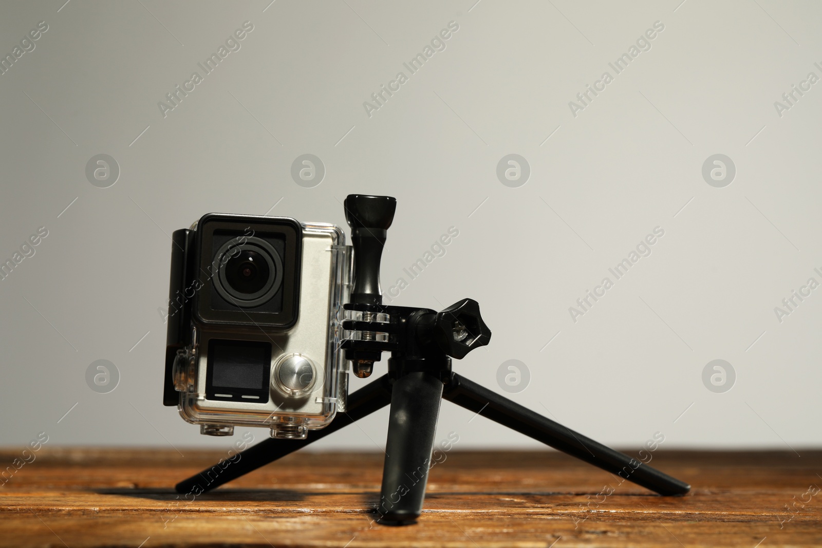 Photo of Modern action camera and tripod on wooden surface against grey background. Space for text