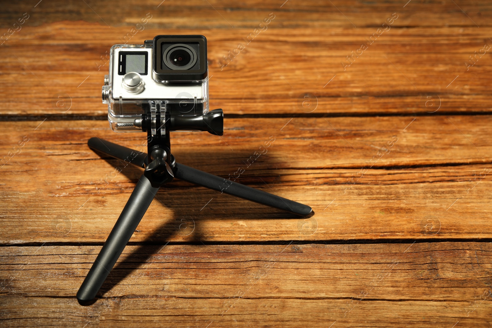 Photo of Modern action camera and tripod on wooden surface. Space for text