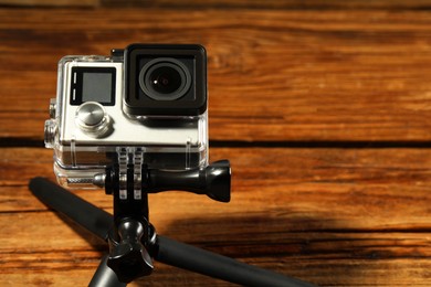 Photo of Modern action camera and tripod on wooden surface, closeup. Space for text