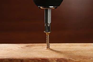 Photo of Screwing screw into wooden plank against brown background, closeup