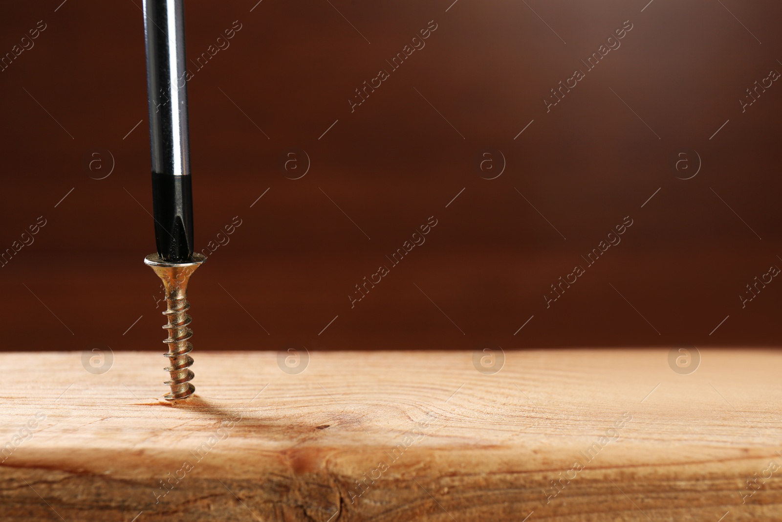 Photo of Screwing screw into wooden plank against brown background, closeup. Space for text