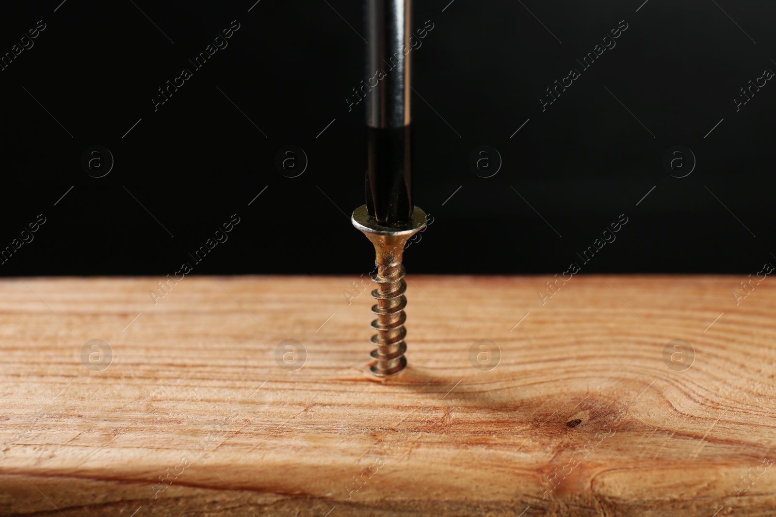 Photo of Screwing screw into wooden plank against dark background, closeup