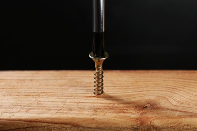 Photo of Screwing screw into wooden plank against dark background, closeup